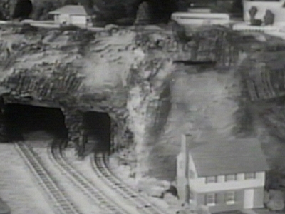 Left Tunnel Area This view shows the tunnel area at the left side of the layout prior to the placement of a circus to the right as shown in the Buckage photos. The residence appears to be a Skyline Models 604 "O Gauge" residence. While other tunnels got portals as the layout progressed to completion, I have seen no evidence that these tunnels ever progressed beyond the stage in which they are shown in this photo.