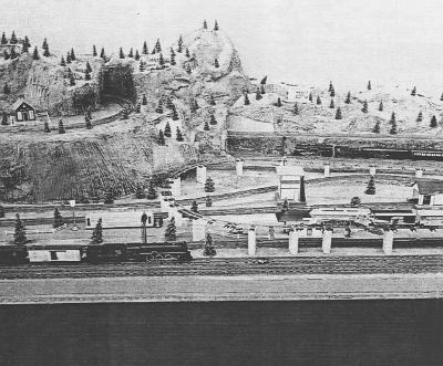 Elevated Loop In the top left area of this photo, the right end of the newly added elevated S gauge loop can be seen entering a tunnel. In the foreground, you can see a Silver Bullet passenger set coming into the right end of the lake area elevated loop. This is the same area which would later be featured on the cover of the 1957 catalog, with a trestle set substituted for the blocks which support the elevated track in this photo.