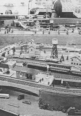 Elevated Station & Industrial Area At the far right end of the layout, we see what used to be the industrial area between the concrete walls is probably still an industrial area, though the buildings are less clearly industrial in nature. The elevated station area is much the same as when the layout was originally built. The mirrors on the back walls give a much different effect than the New York City backdrop that previously covered the back wall of this area. Interestingly, we get an exceptionally good view of some of the things we can't see on the layout in the direct view and also of the display shelves on the other side of the room.